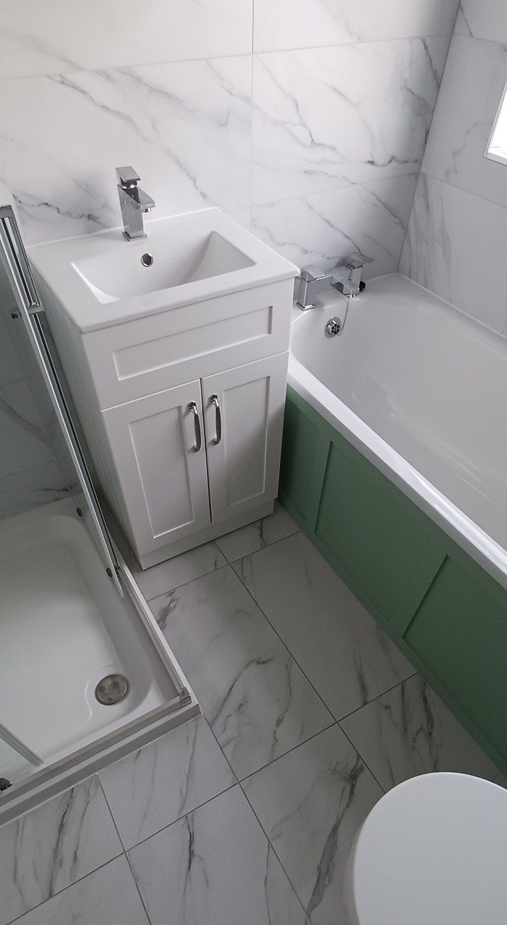 A finished bathroom: shaker vanity, panelled bath in sage green, marble-effect tiles